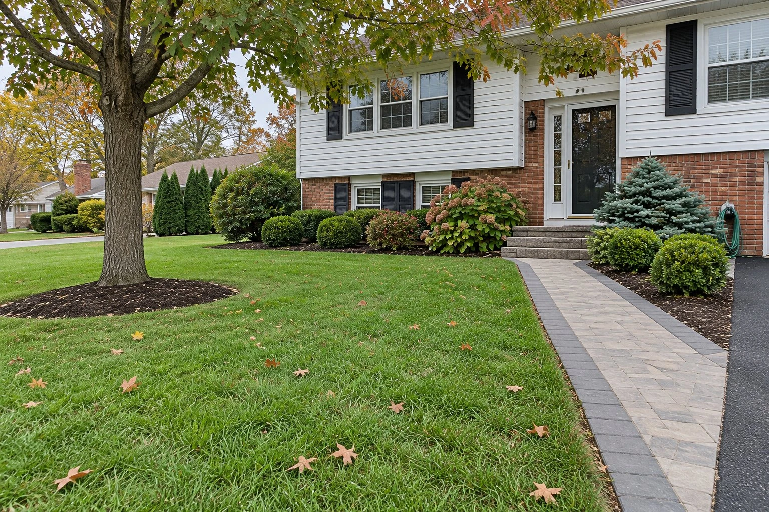 Grey paver front walk and mulched beds in front of a brick bi-level house with black shutters